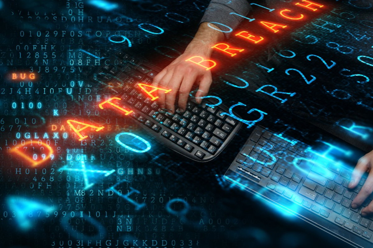 Hands typing on two keyboards beneath glowing orange DATA BREACH lettering on a background of blue binary digits.